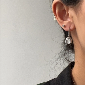 Detail of minimalist silver-toned hoop earring with an oval white shell pendant on a model