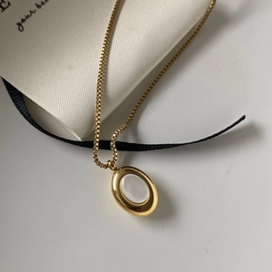 Macro detail of oval gold pendant with white shell inlay and box chain on silk ribbon