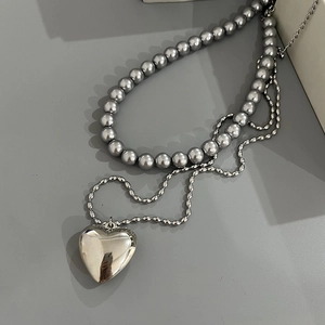 Detail of grey pearl double-layer necklace with hollow heart pendant and metal wave chain
