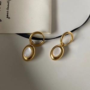 Detailed close-up of 18K gold-plated oval white shell drop earrings on a minimalist background
