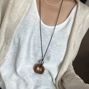 Dettaglio di un ciondolo ad anello in osso di cammello su cordino nero con t-shirt bianca