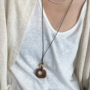 Dettaglio di una collana lunga con pendente rotondo marrone e perline dorate su nero