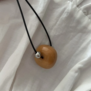 Détail d'un pendentif en résine ambrée avec cordon noir et perles métalliques argentées