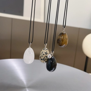 Vertical view of four egg-shaped natural stone pendants including obsidian and tiger eye