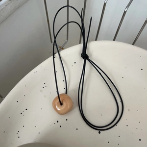 Détail du collier minimaliste en acier inoxydable avec pendentif anneau ivoire sur cordon noir