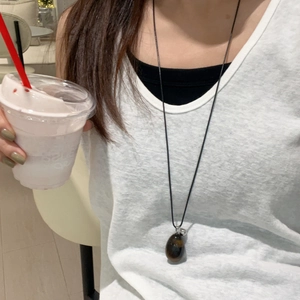 Long necklace with egg-shaped brown tiger eye stone pendant worn in a casual lifestyle setting