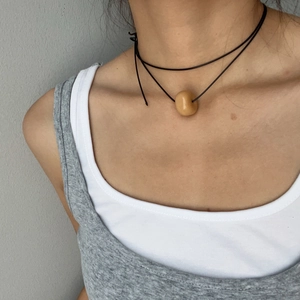 Gros plan d'un collier minimaliste avec pendentif rond lisse sur un cordon noir