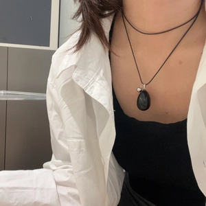 Close-up of a teardrop-shaped black natural stone pendant necklace worn by a model