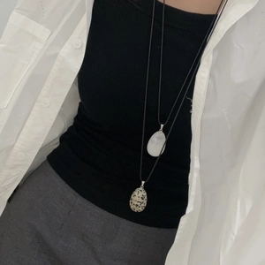 Detail view of long stone pendants on a black cord worn over a gray sweater