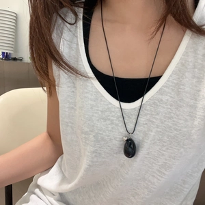 Detail of a smooth black egg-shaped stone pendant on a necklace worn by a model