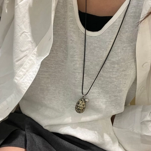 Minimalist egg-shaped spotted stone pendant necklace on long black cord worn with white shirt