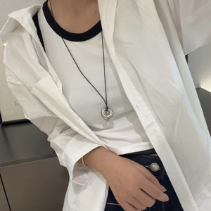 Detail of silver hollow heart pendant on a black cord necklace worn with casual clothes