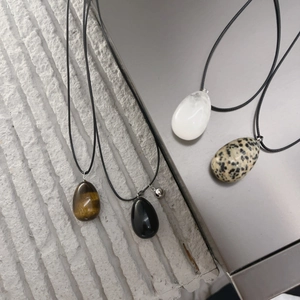 Close-up of four egg-shaped natural stone pendants including tiger eye and obsidian stones
