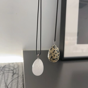 Detail view of two natural egg-shaped stone pendants on black cords in a modern minimalist setting