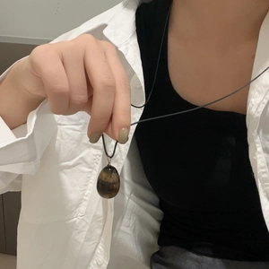 Detailed view of teardrop tiger eye stone pendant on a black cord necklace