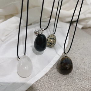 Detailed macro view of smooth egg-shaped natural stone pendants on black cord necklaces