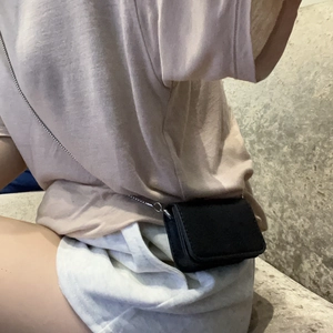 Detail of a mini black leather crossbody bag with a slim silver chain on a model