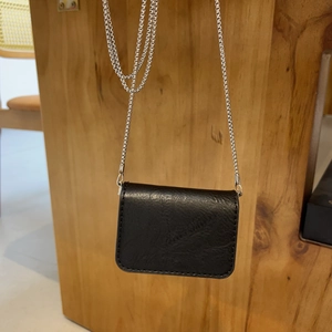Detail of a black mini leather bag with a fine silver chain and textured surface