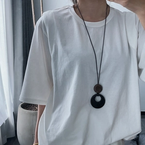 Sautoir rétro en verre noir sur t-shirt blanc ample pour femme sous lumière naturelle