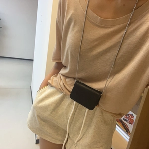 Model wearing a small black leather crossbody bag with silver chain on a beige t-shirt