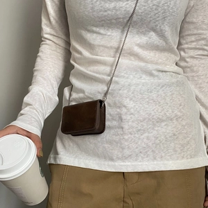 Brown mini crossbody bag with silver chain strap worn over white top and khaki pants