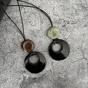 Détail de collier long minimaliste avec anneaux noirs émaillés et perles marbrées