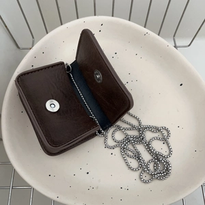 Mini dark brown pebbled leather crossbody bag with silver chain in a decorative dish