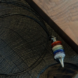 Seven chakra natural stone pendulum necklace with silver metal accents on black wood