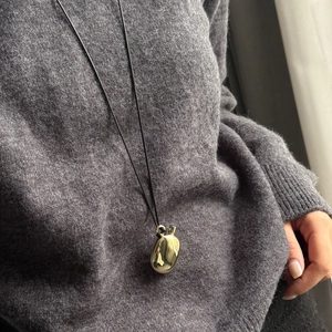 Close-up of minimalist gold pebble pendant on a black cord over a grey knitted sweater