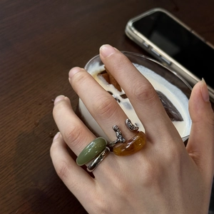 Close-up of a hand wearing green and amber resin rings with silver bands holding a coffee