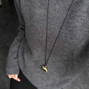Close-up of a polished gold apple pendant on a long black cord necklace over a sweater