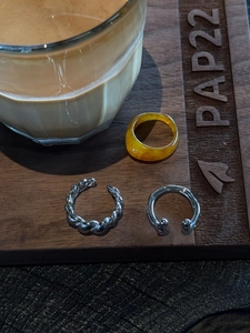 Macro shot of resin amber ring and silver open rings on dark wooden tray with coffee
