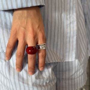 Detail view of a wide resin dome ring in dark red and a textured silver metal ring on fingers