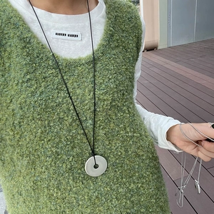 Detail view of minimalist silver hollow pendant on a black cord over a green sweater
