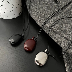 Three minimalist pebble pendants in black, amber red, and silver on black wood