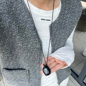 Detail of minimalist black mirror oval pendant worn over a grey tweed waistcoat
