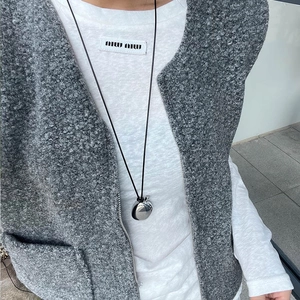 Polished silver sphere pendant necklace worn on a model with a grey textured vest