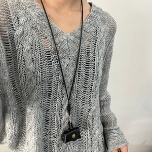 Halskettendetail mit einer Mini-Ledergeldbörse in Schwarz auf einem grauen Strickpullover