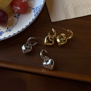 Detailed macro view of gold and silver heart-shaped pendant hoop earrings on a wooden tray