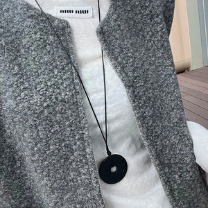 Close-up of minimalist black donut pendant necklace on grey wool coat and white shirt