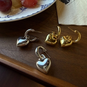 Chunky gold and silver heart hoop earrings with polished mirror finish on dark wood