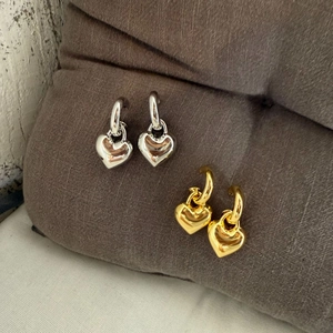 Detailed view of gold and silver heart charms on C-shaped earrings over brown fabric