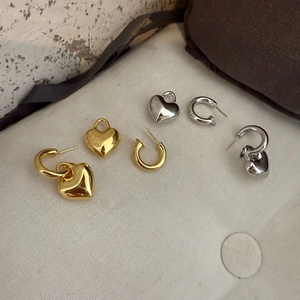 Detailed view of polished gold and silver heart earrings set on textured fabric