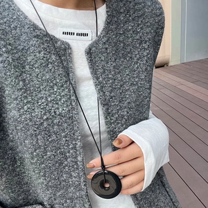 Detail of a minimalist black round pendant necklace worn on a textured grey waistcoat