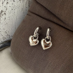 Macro shot of polished gold-plated heart pendant earrings on a brown knit background