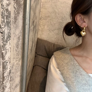 Detailed close-up of golden heart pendant hoop earrings worn by a fashion model