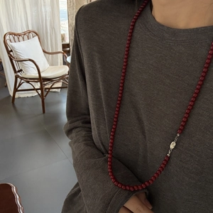 Detail of long red bead necklace with silver clasp worn over a grey sweater garment