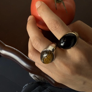 Detalle de anillos retro con ojo de tigre y obsidiana negra en la mano de una modelo