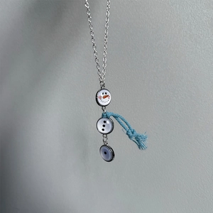 Detail van een sneeuwpop hanger ketting met zilveren ketting en blauwe lint sjaal accent