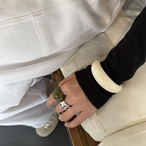 Dettaglio di anelli in resina verde oliva e bracciale bianco indossati sulla mano